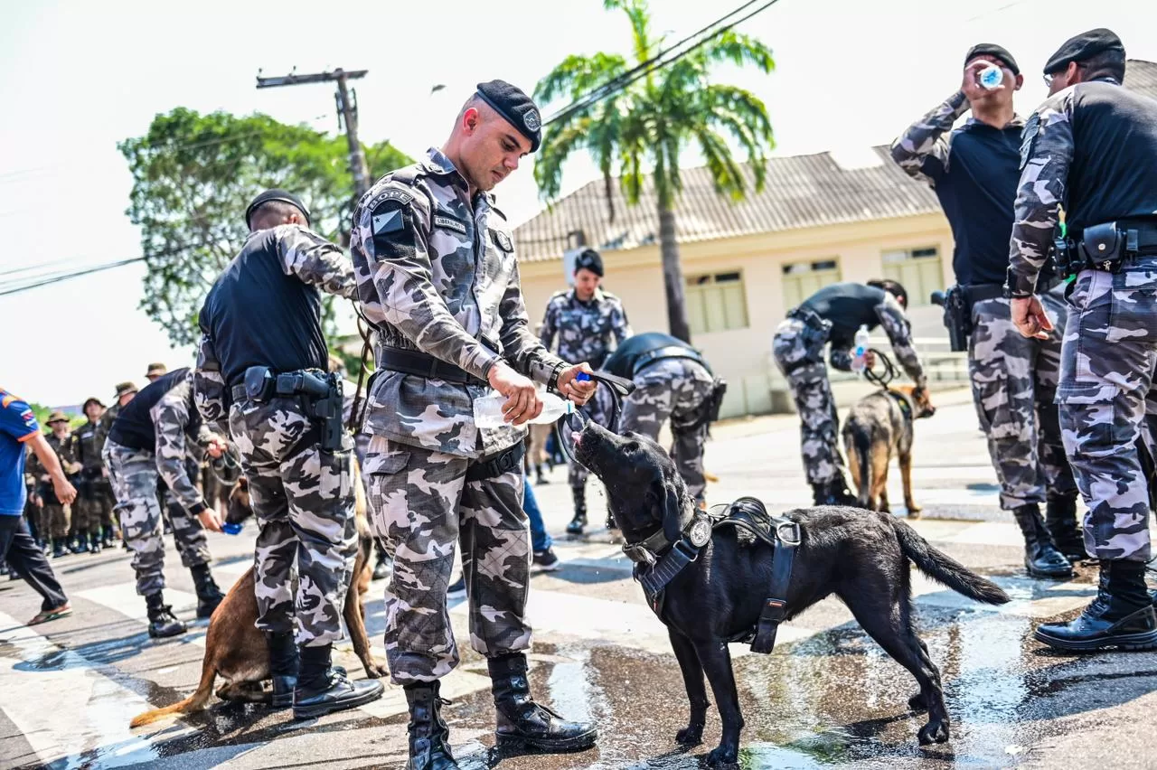 Com sensação térmica de 38°C, policiais se refrescam e seguram cães do BOPE no braço