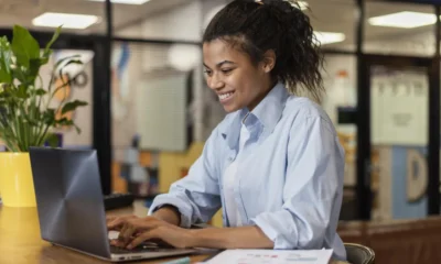 vista-lateral-de-uma-mulher-sorridente-trabalhando-com-um-laptop-no-escritorio