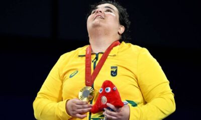 Uma atleta vestindo uma camisa amarela com detalhes verdes, segurando uma medalha dourada e um boneco vermelho. Ela está olhando para cima, com uma expressão de alegria e emoção. A medalha está pendurada em seu pescoço por uma fita vermelha.
Brasileira Rebeca Silva comemora ouro durante cerimônia de premiação da categoria J2 acima de 70 kg - Jennifer Lorenzini/Reuters
